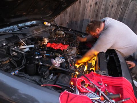 2003 Ford Crown Victoria - Worker leans deep into an open engine compartment lit by a yellow work light, wrenches resting on a red rag.