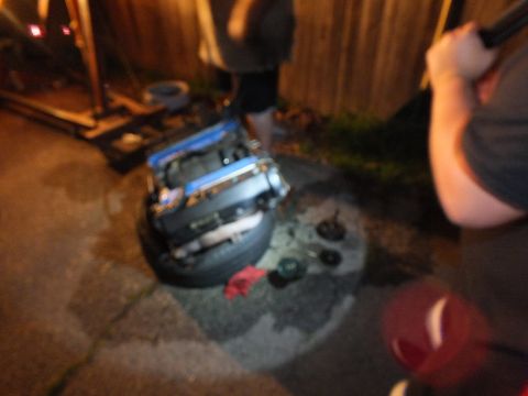 2003 Ford Crown Victoria - Disassembled V6 sits on a tire in a dim alley, loose components spread across damp concrete