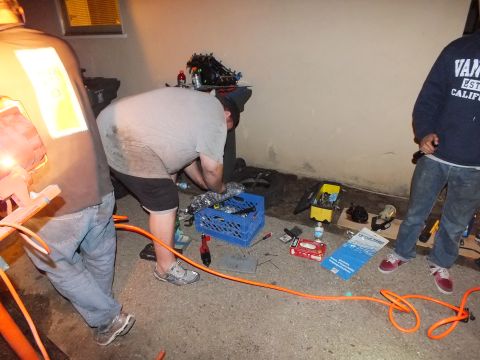 2003 Ford Crown Victoria - Worker sorts components from a blue crate on a garage floor while a bystander in a hoodie looks on