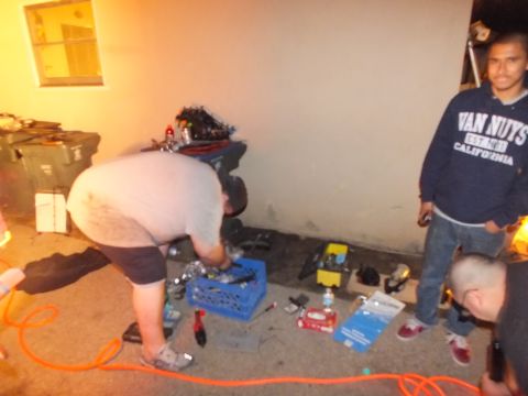 2003 Ford Crown Victoria - Bystander wearing a Van Nuys California hoodie stands by as a man works over parts on the floor