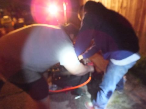 2003 Ford Crown Victoria - Blurred night shot of two men leaning over an engine on a tire, lit by a harsh camera flash