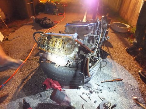 2003 Ford Crown Victoria - V6 short block with exposed cam and chain rests on a tire, loose bolts littering the wet ground