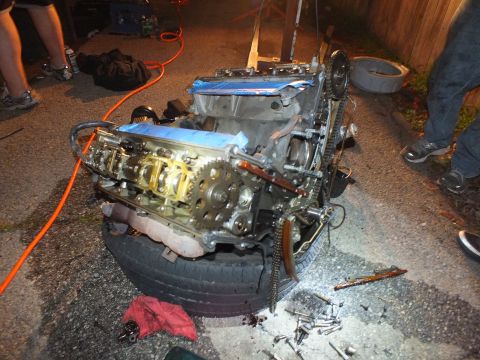 2003 Ford Crown Victoria - Open V6 showing camshafts and timing chain sits angled on a tire during a nighttime teardown