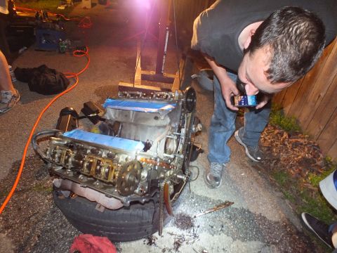 2003 Ford Crown Victoria - Worker photographs the exposed V6 on a tire with his phone under portable lighting at night