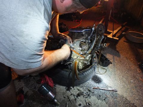 2003 Ford Crown Victoria - Capped worker reaches into the timing area of a V6 on a tire, tools scattered on the pavement