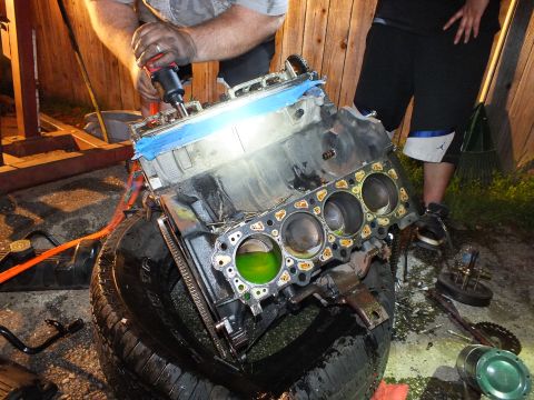 2003 Ford Crown Victoria - Worker runs a red cordless drill on a stripped block on a tire, green coolant in the open cylinders