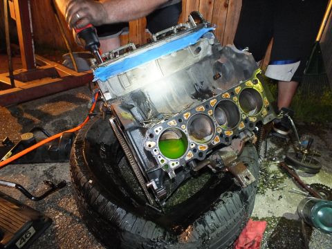 2003 Ford Crown Victoria - Bare block with four bores and a green-coolant cylinder sits on an oily tire during the teardown