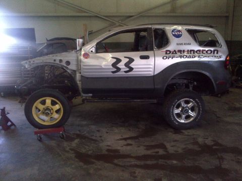 1999 Isuzu Vehicross - This modified SUV is in a garage, undergoing repairs or modifications, with racing decals visible on its side.