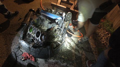 2003 Ford Crown Victoria - V6 with exposed bores sits on a tire under flashlight as a worker sprays or cleans alongside it