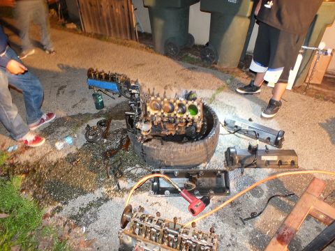 2003 Ford Crown Victoria - People work around an oily engine block balanced on a tire during a late-night teardown