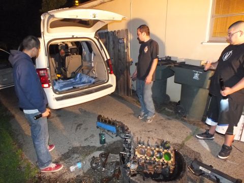 2003 Ford Crown Victoria - Three men stand near an open-hatch minivan over a disassembled engine in a dim driveway