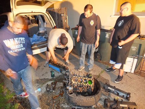 2003 Ford Crown Victoria - Group works on an engine block resting on a tire, one wearing a Van Nuys California hoodie