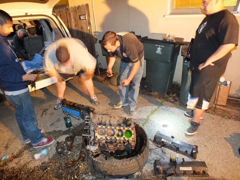 2003 Ford Crown Victoria - Several men crouch and stand around an engine block on a tire with parts scattered nearby