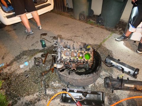 2003 Ford Crown Victoria - Disassembled engine sits on a tire surrounded by valve covers and components in the dark