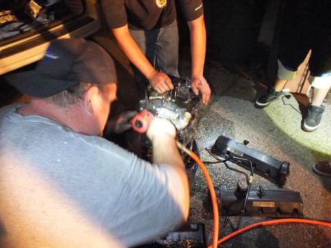 2003 Ford Crown Victoria - Two men work an engine with a pneumatic tool and orange air hose under low light