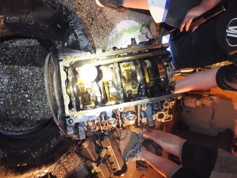 2003 Ford Crown Victoria - engine block stands on a tire with crankshaft and rods exposed under a worklight