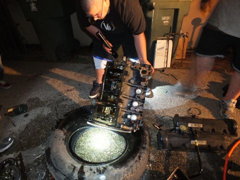 2003 Ford Crown Victoria - worker hoists an engine block above a tire while holding a flashlight in the driveway