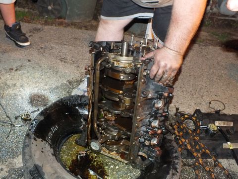 2003 Ford Crown Victoria - Hands steady an open engine block over a tire, crankshaft and main bearing caps visible