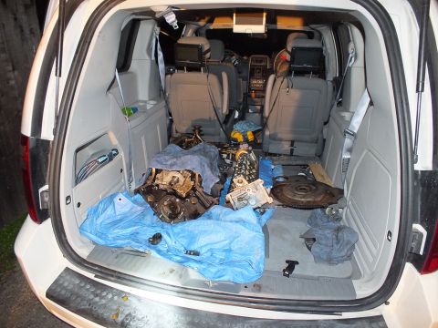 2003 Ford Crown Victoria - View into a minivan's folded rear seats showing engine block, flywheel and scattered parts