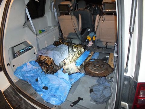 2003 Ford Crown Victoria - Engine components and a rusty flexplate spread across tarps in a minivan rear interior with rear hatch open