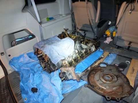 2003 Ford Crown Victoria - Engine sitting upright with intake manifold exposed beside a rusty flexplate on blue tarp in a vehicle cabin