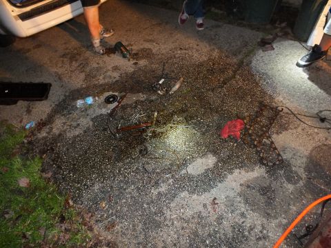 2003 Ford Crown Victoria - Bike frame, wheel and scattered parts on a wet gravel surface lit by flashlight next to a parked van at night