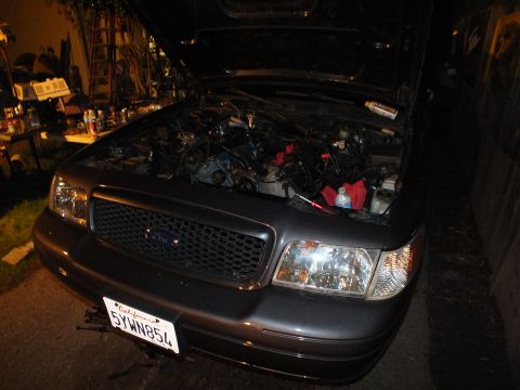 2003 Ford Crown Victoria - Dark Ford Crown Victoria with raised hood and exposed engine bay in a cluttered garage, California license 5YWN854
