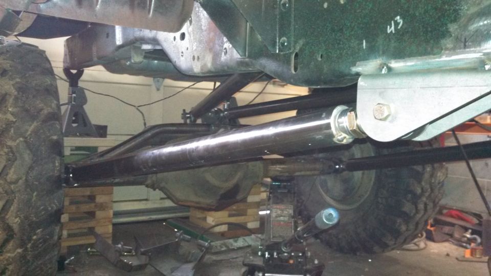 Underside of a truck chassis with large tires, suspension links, and jack stands visible