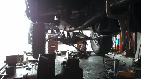 1967 Ford F-250 - A truck's undercarriage is shown with suspension work in progress, supported by jacks and blocks.