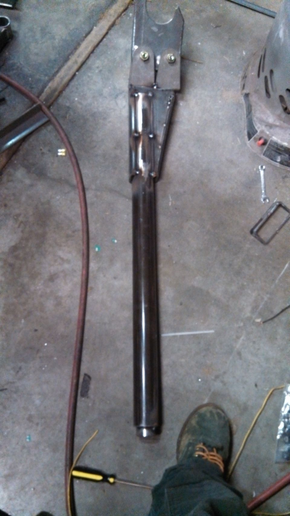 Fabricated metal suspension component with two bolts at the top, lying on a concrete floor