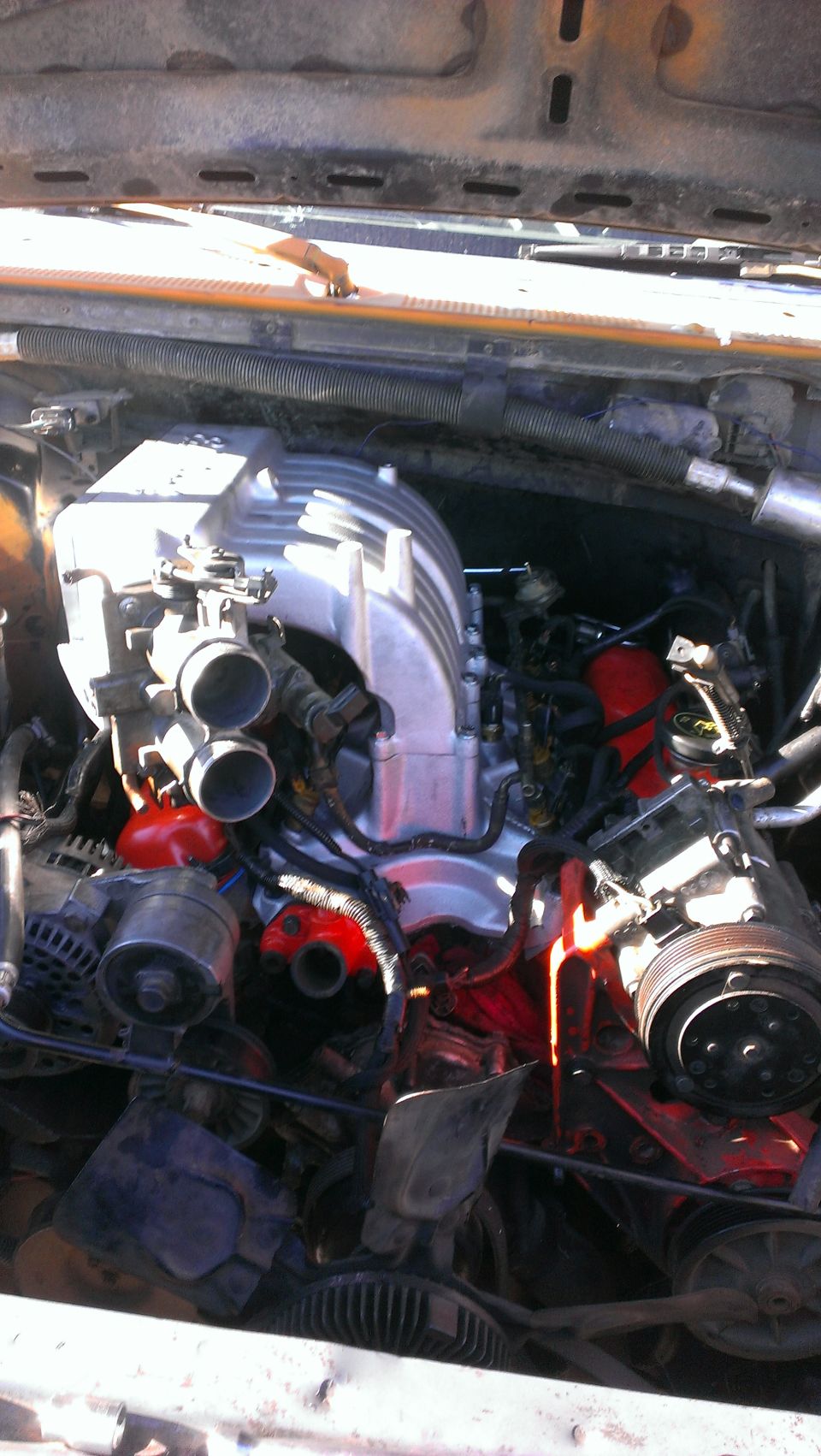 Engine bay with a large, silver aftermarket intake manifold and red engine block components