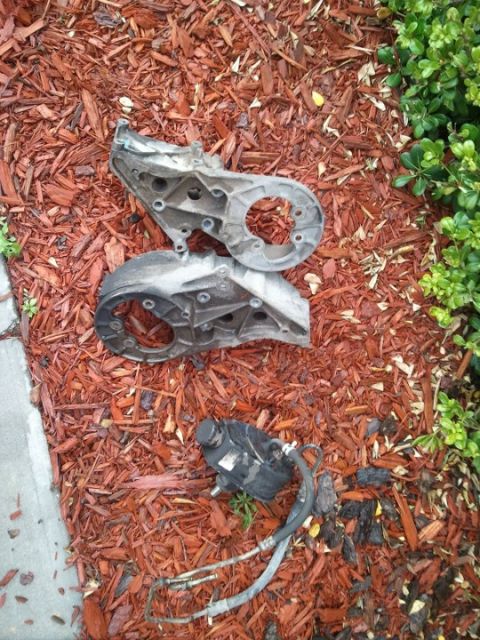 1994 Ford Bronco - Engine parts, including brackets and a power steering pump, are displayed on a bed of mulch.