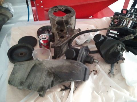 1994 Ford Bronco - Various power steering components, including a pump, bracket, and pulley, are laid out on a surface next to a soda can.