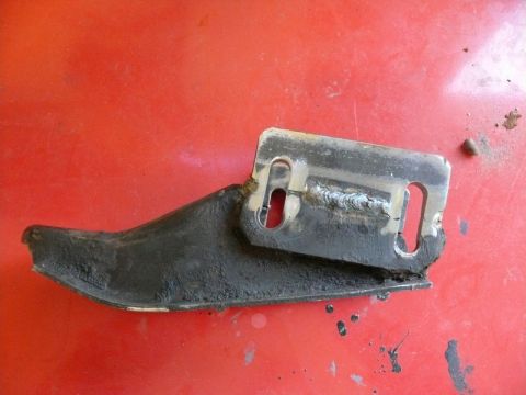 1976 Chevrolet Corvette - A close-up view of a metal bracket with visible welds and mounting slots against a red background.