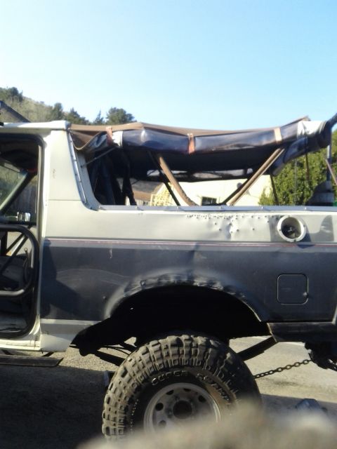 1991 Ford Bronco - Side view of a damaged Ford Bronco with a soft top removed, revealing its internal frame.