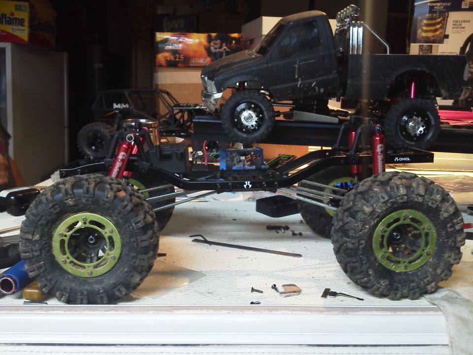 RC truck chassis with large tires and a black pickup body on top, viewed from the side