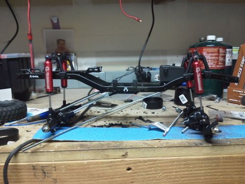 1985 Ford Bronco - The chassis of a remote-controlled car is shown on a workbench, with various parts and tools scattered around.