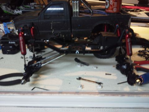 1985 Ford Bronco - A disassembled black pickup truck chassis is on a workbench with tools and parts.