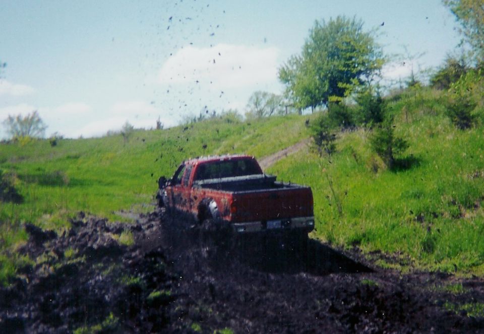 Red extended-cab pickup throwing mud while running through a mud pit below a grassy hill