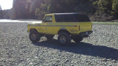 1978 Ford Bronco - A yellow 1978 Ford Bronco with a black top sits on a rocky surface near a body of water.