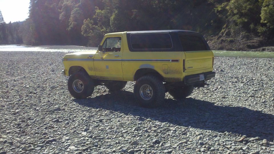 Yellow 1978 Ford Bronco with black top parked on a rocky shore