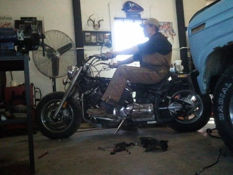 1995 Ford F-150 - A man sits on a motorcycle in a workshop, with tools on the floor and a truck nearby.