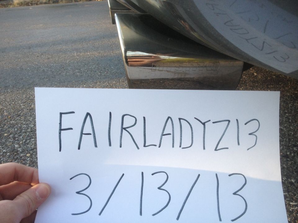 Paper with 'FAIRLADYZ13 3/13/13' written on it, held in front of a vehicle's exhaust tip