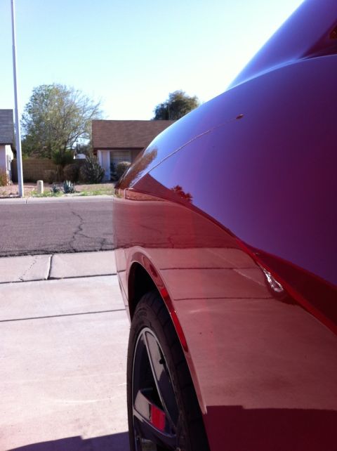 2010 Dodge Challenger - Side view of a red car, focusing on the fender and a portion of the hood, with a residential background.