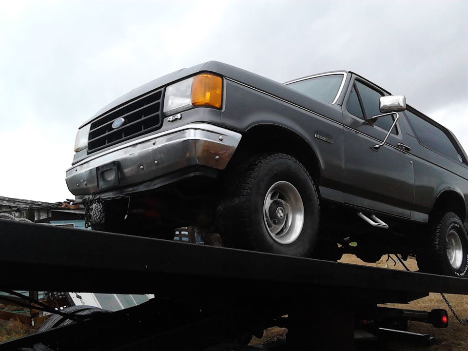 Gray 1987 Ford Bronco on a flatbed truck, front 3/4 view