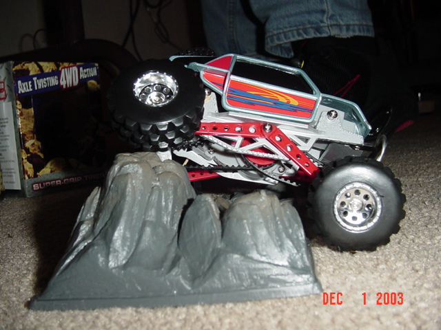 RC rock-crawler with blue-and-red body on molded plastic rocks, box reading Axle Twisting 4WD, Dec 2003