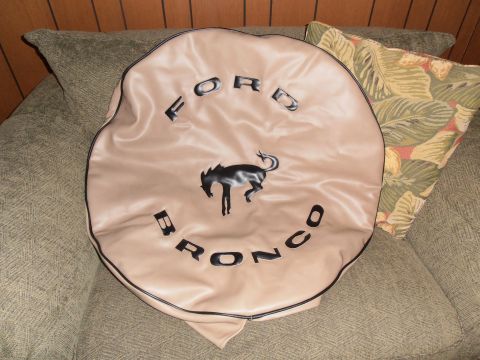 1990 Ford Bronco - A tan tire cover the Ford Bronco emblem and lettering is displayed on a couch.