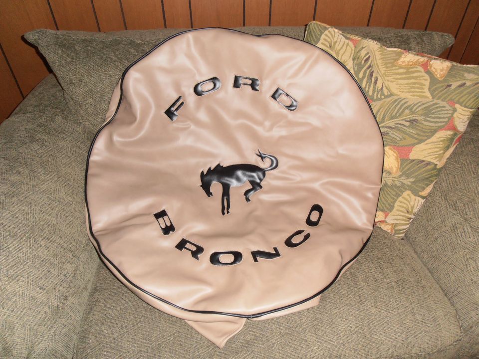 Tan tire cover with black Ford Bronco logo and text, resting on a couch