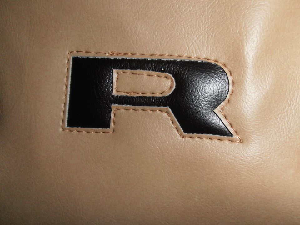 Embroidered black letter R on tan material, possibly from a car seat cover or tire cover
