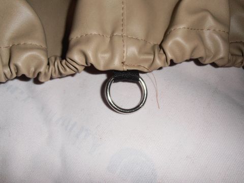 1990 Ford Bronco - Close-up of a tan tire cover showing its elastic edge and a metal grommet for attachment.